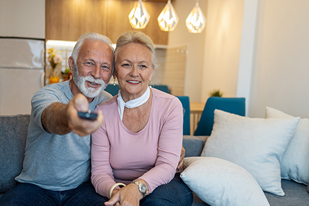 senioren_bungalows_podersdorf_paar_mobile Älteres Paar mit Fernbedienung auf der Couch sitzend im SeniorenBungalow Podersdorf klein
